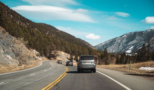 Free Cars driving on a winding mountain road surrounded by scenic views of trees and blue sky. Stock Photo