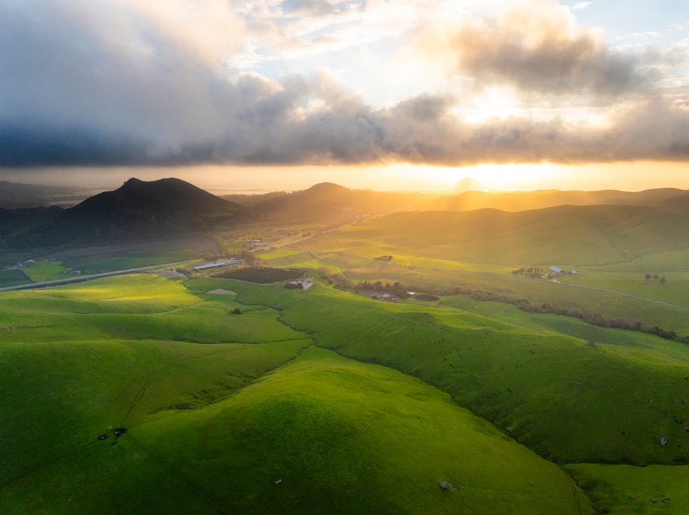 The sun is setting over a green field with hills