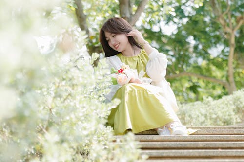 Cute Woman in Green Dress Sitting on Stairs in Park