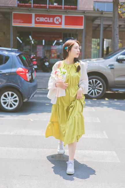 Fashionable woman in a green dress crosses a city street on a sunny day.