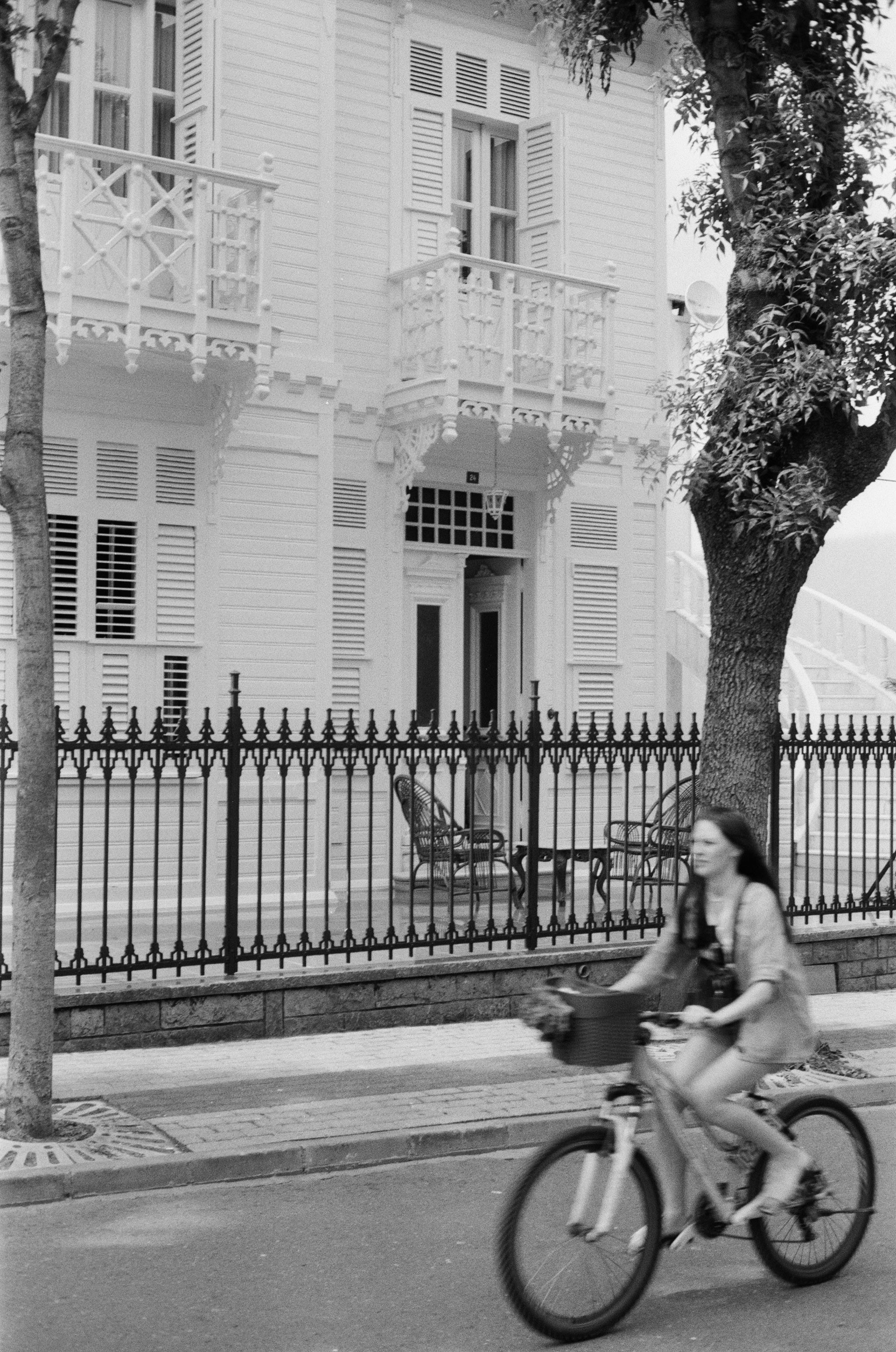 A woman cycles past a historic mansion in İstanbul, captured in monochrome.
