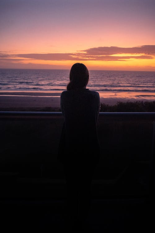 A woman looking out at the ocean at sunset