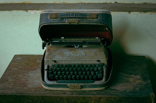 A rustic and nostalgic Remington typewriter in a weathered case on a wooden table.