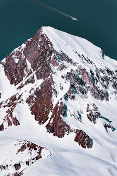 Epic aerial shot of a snowy mountain summit with an airplane flying overhead.