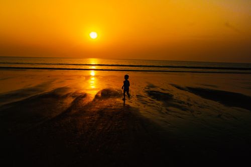 Free Silhouette of a child running on a Mumbai beach during a vibrant sunset. Stock Photo