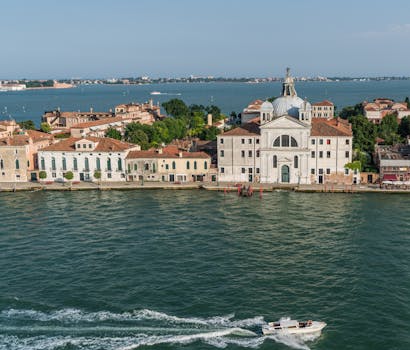 从鸟瞰视角看，一个宁静的岛屿上矗立着经典的威尼斯建筑，周围环绕着清澈的蓝色海水