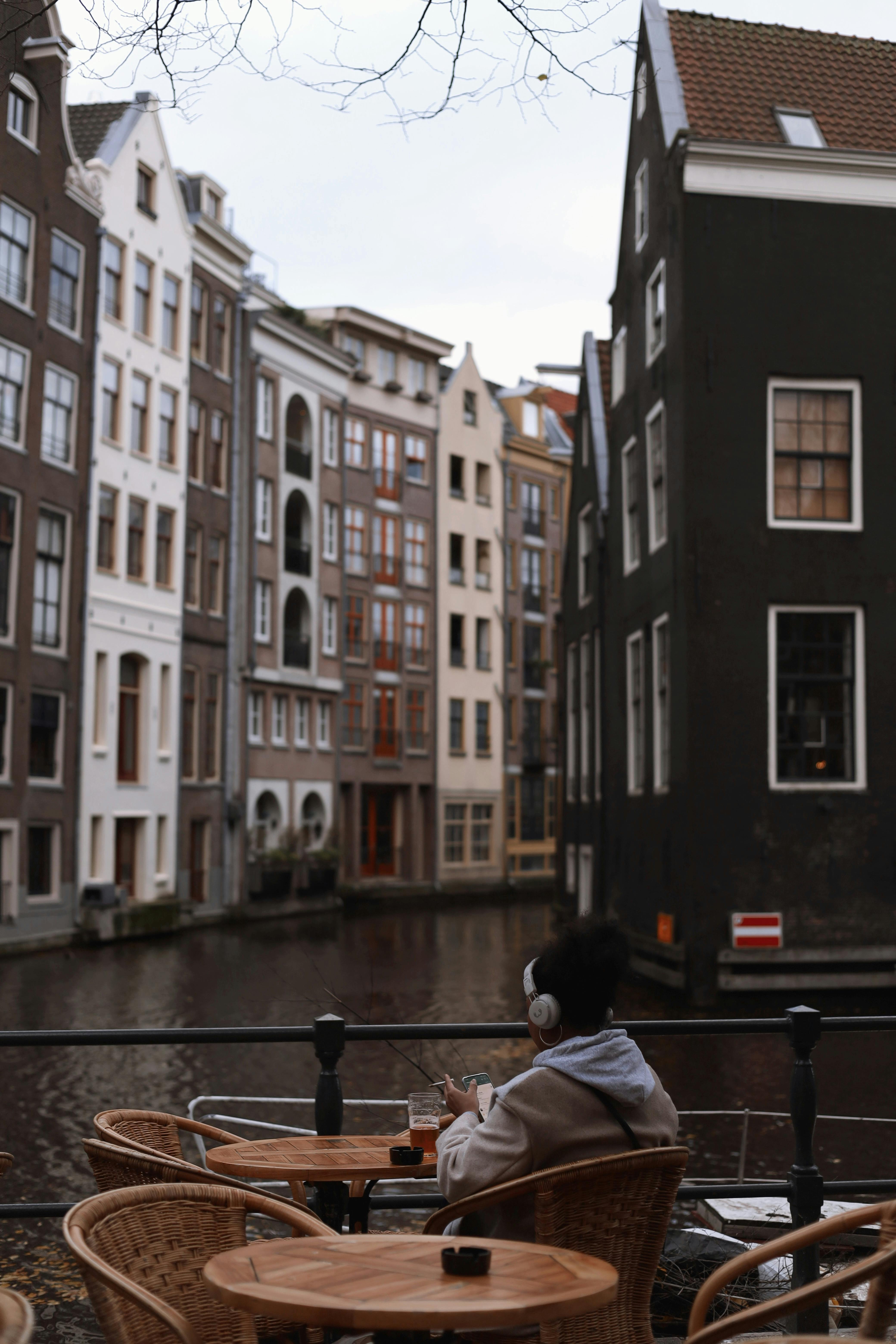 A woman sits at a café overlooking the historic Amsterdam canal houses.