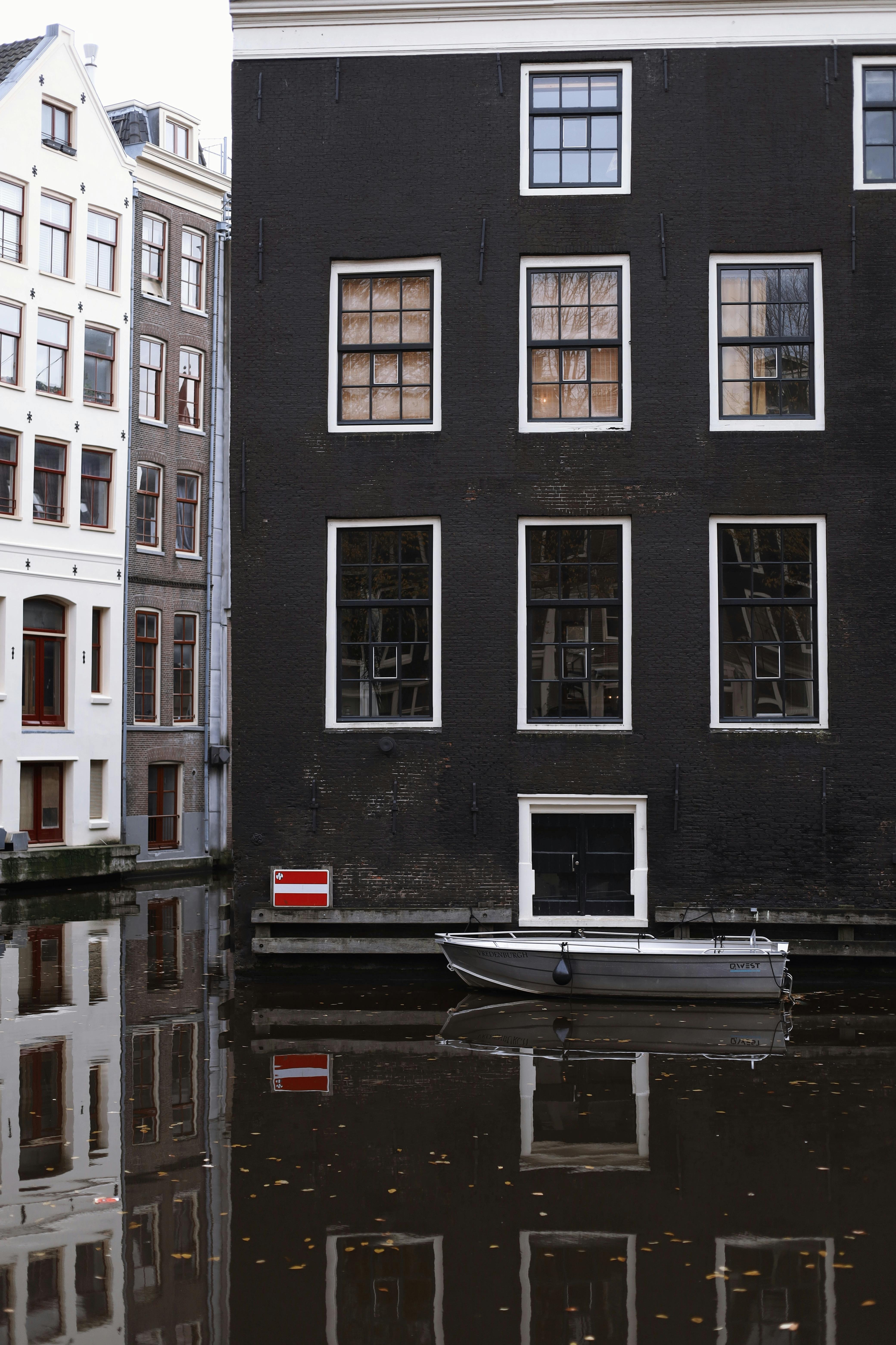 Charming canal houses with reflections in Amsterdam, showcasing beautiful urban architecture and a motorboat.