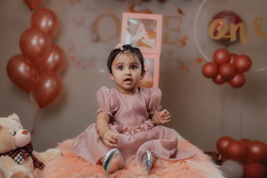 Cute baby girl in a pink dress with balloons and teddy bear at her birthday party.