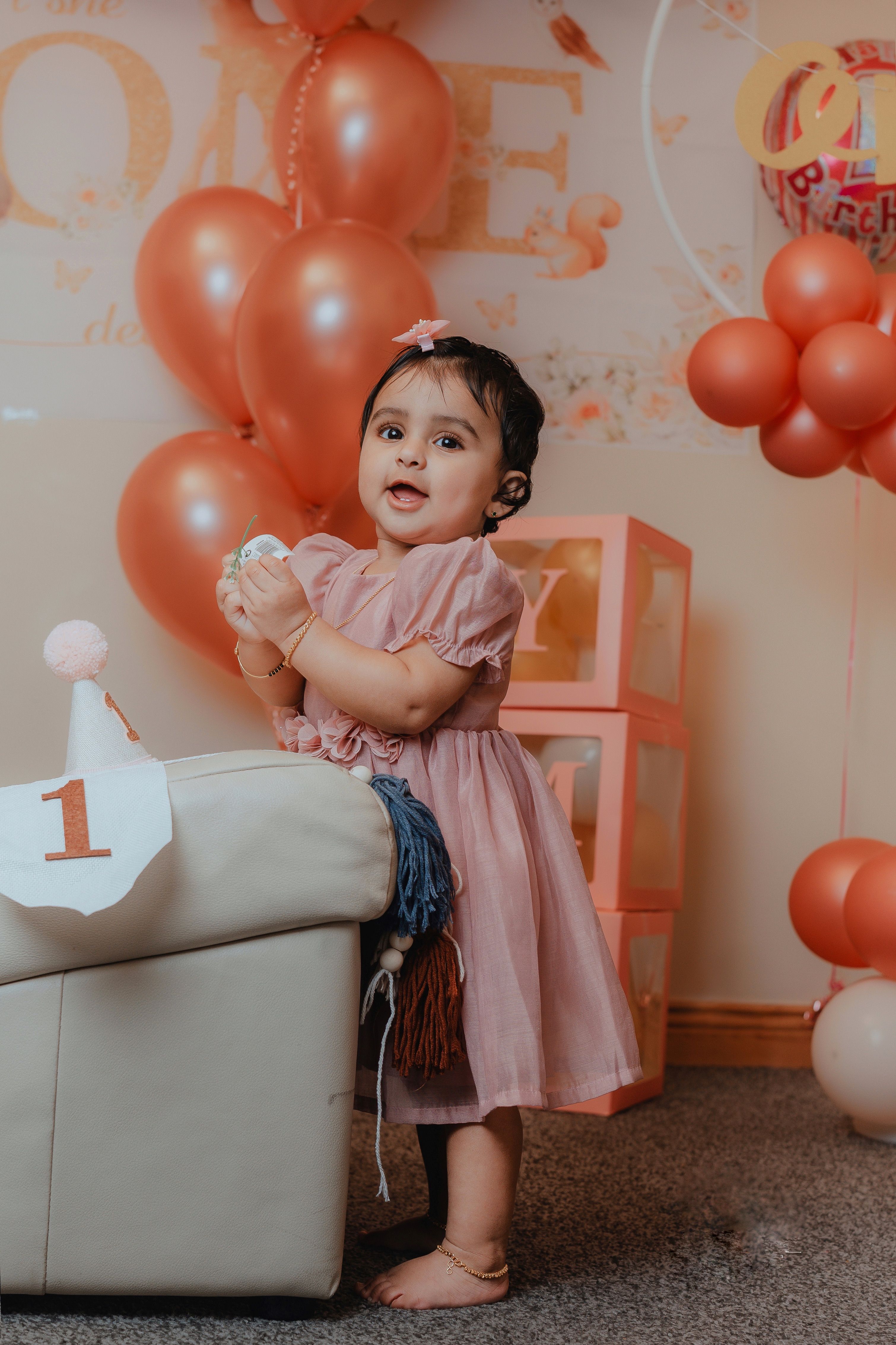 Charming photo of a little girl in a pink dress enjoying her first birthday with balloons.