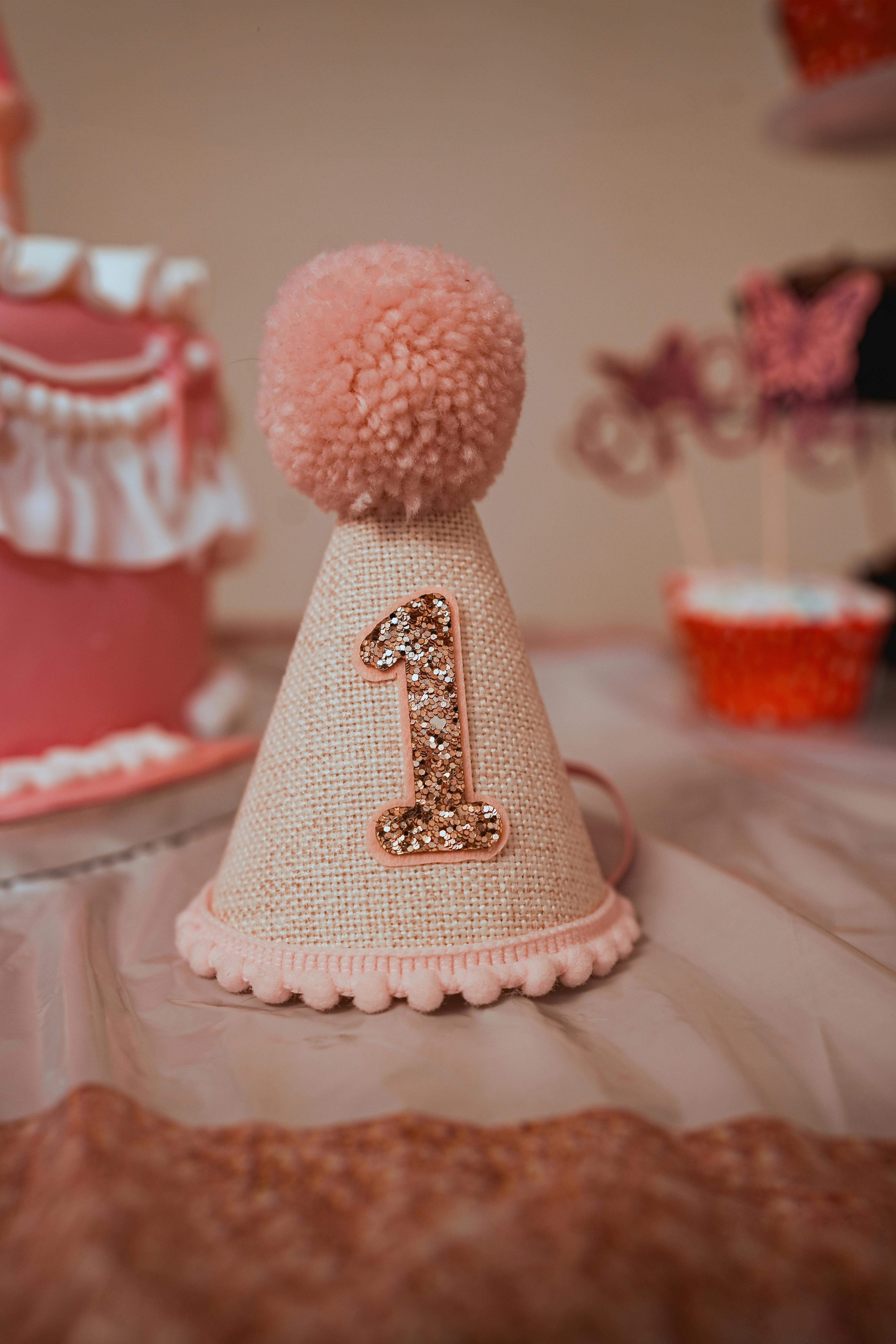 Celebrate a first birthday with this charming pink party hat featuring a shiny number one.