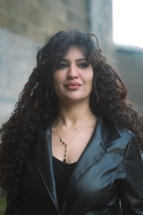 Free Portrait of a confident woman in a leather jacket with curly hair, smiling softly outdoors. Stock Photo