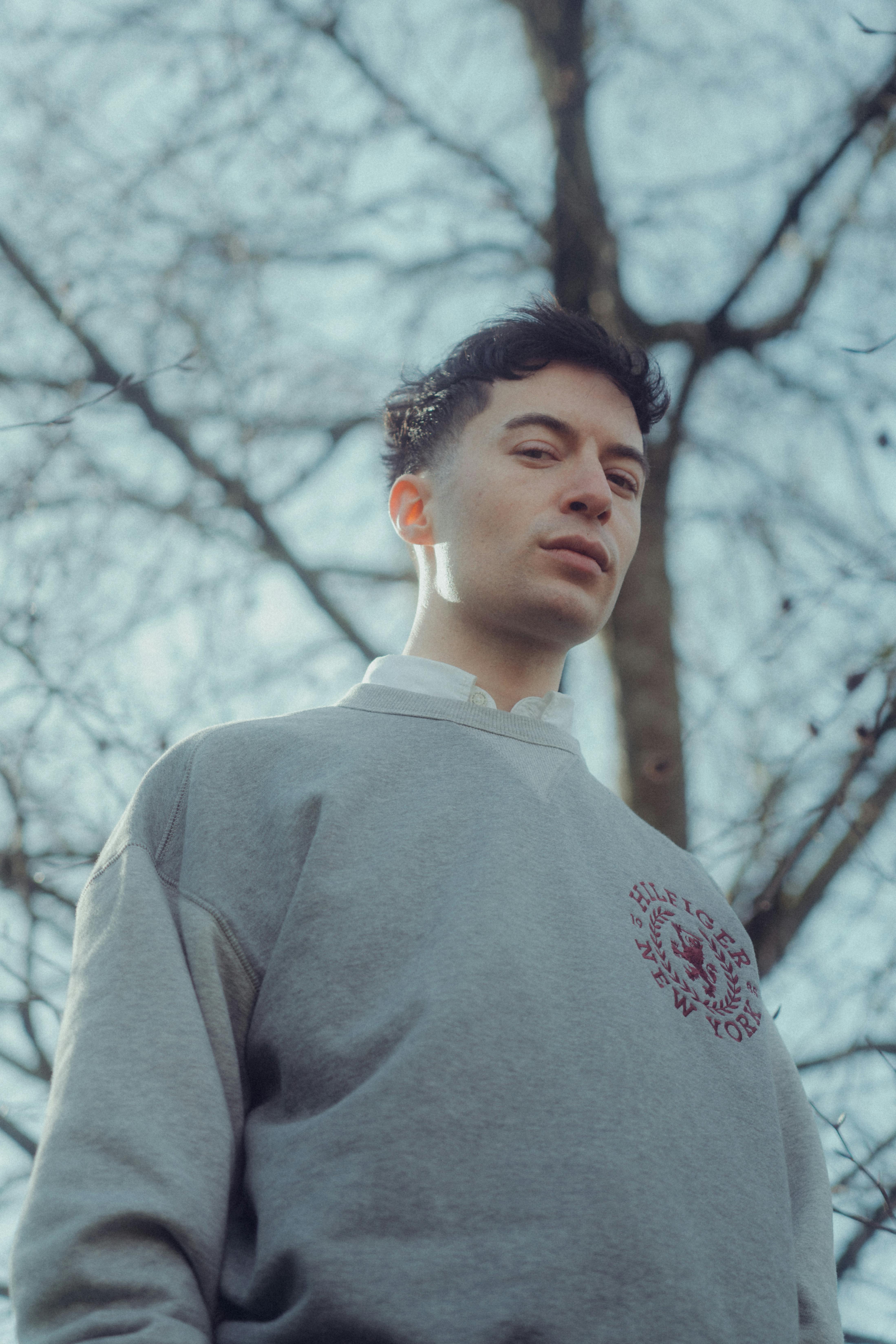 Fashionable young man posing confidently outdoors with trees in spring.
