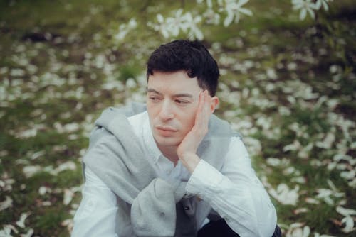 A man in a white shirt and grey sweater sitting on the ground