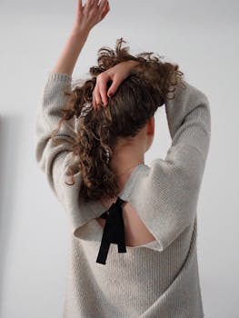 A fashion-forward woman adjusts her hair while wearing a stylish sweater in a studio setting.
