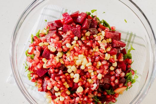 Colorful salad with pomegranate, corn, and beets in a glass bowl.