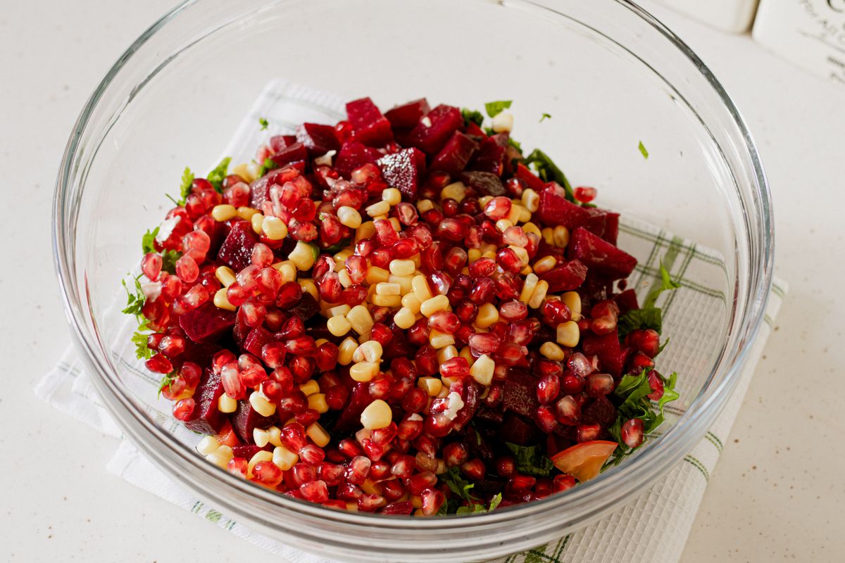Glass bowl of diced beets, pomegranate seeds, corn kernels and parsley on a white towel