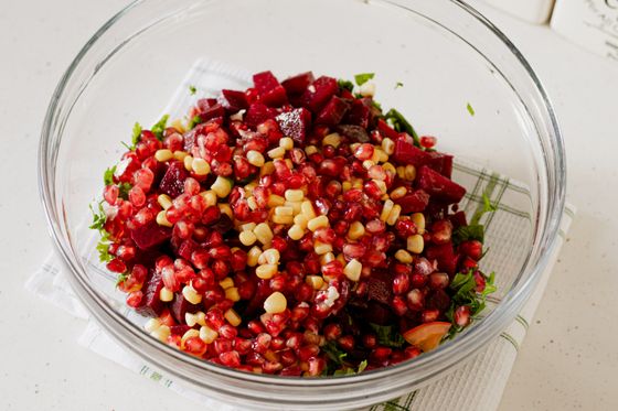 Glass bowl of diced beets, pomegranate seeds, corn kernels and parsley on a white towel