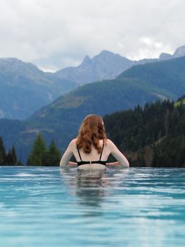 Woman in a pool enjoying a scenic mountain view, evoking relaxation and tranquility.