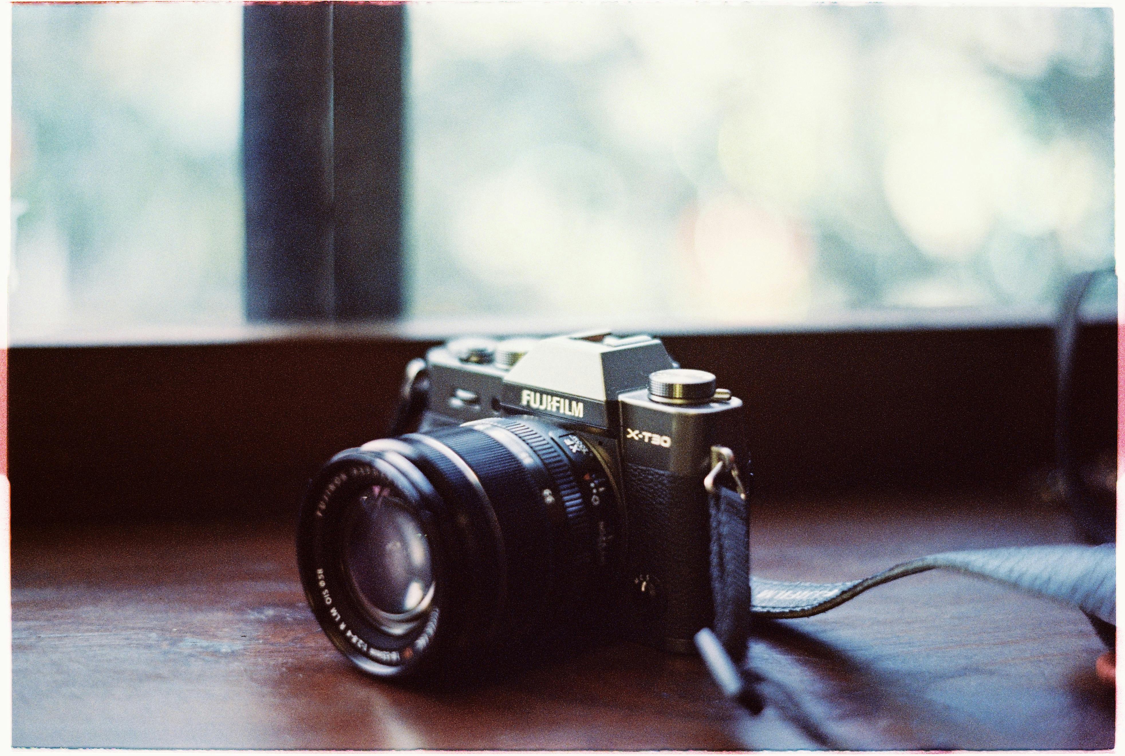 A classic Fujifilm camera resting on a wooden surface by a window, capturing a retro aesthetic.
