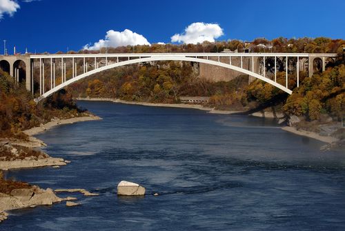Free Panoramic view of Rainbow Bridge over the river in fall with vibrant foliage and blue sky. Stock Photo