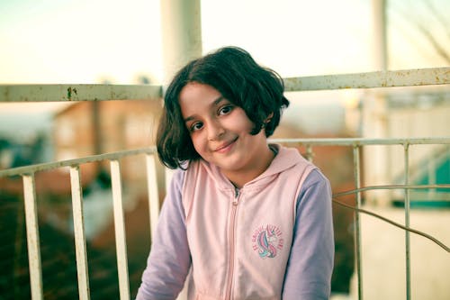 A young girl smiles while sitting on a balcony