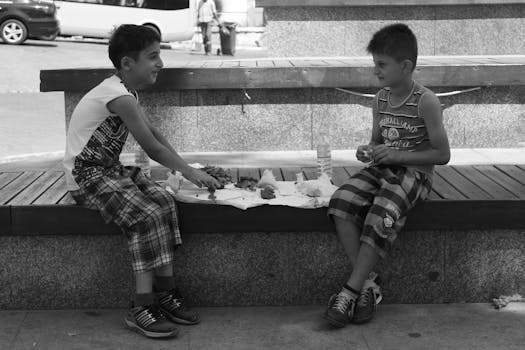 Two boys enjoying snacks on a park bench in a lively outdoor setting.