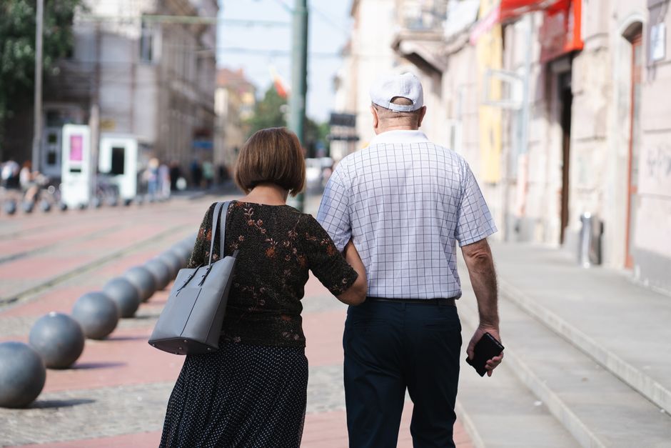 Pareja de ancianos caminando de la mano por una soleada calle urbana, capturando un momento de unión.
