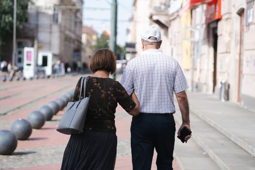 Free Senior couple walking arm-in-arm on a sunny urban street, capturing a moment of togetherness. Stock Photo