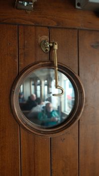 View through a ship's porthole showcasing passengers inside a vintage wooden ferry.