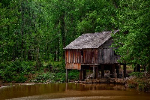 Free A scenic view of a rustic water mill surrounded by lush greenery at daytime. Stock Photo