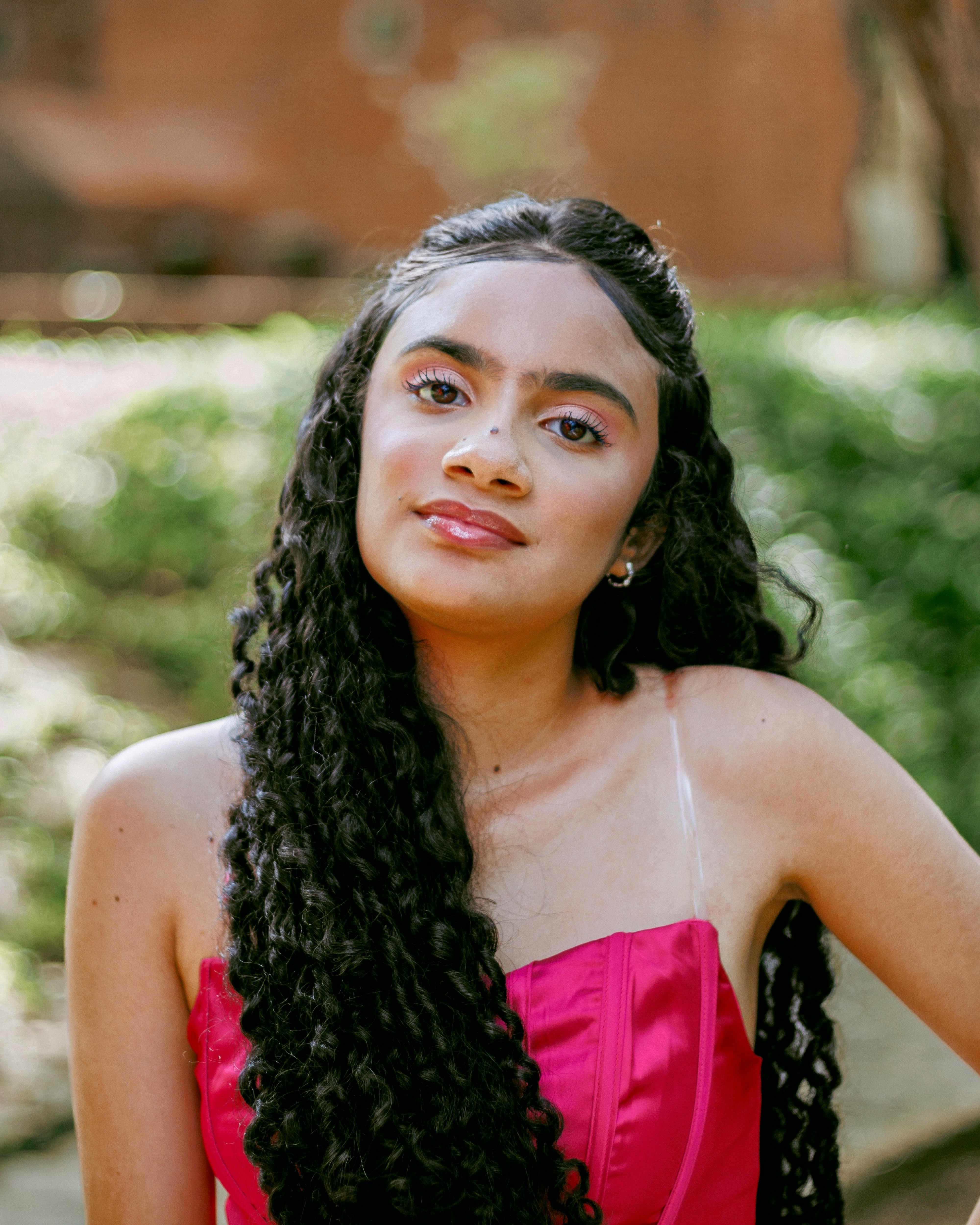 Charming portrait of a woman with curly hair wearing a pink dress outdoors.
