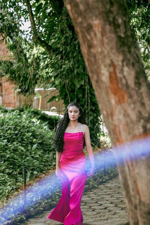 A woman in a pink dress is standing in front of a tree