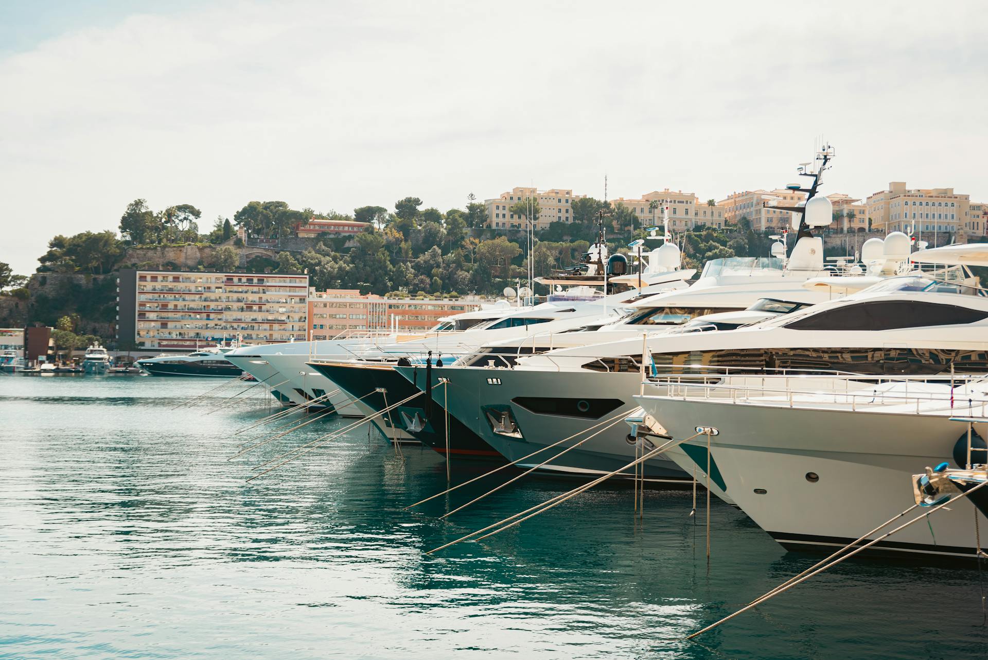 A scenic view of luxury yachts moored in Monaco harbor with cityscape in the background.