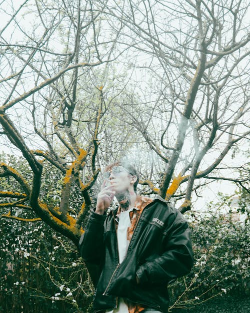 A man smoking a cigarette in front of a tree