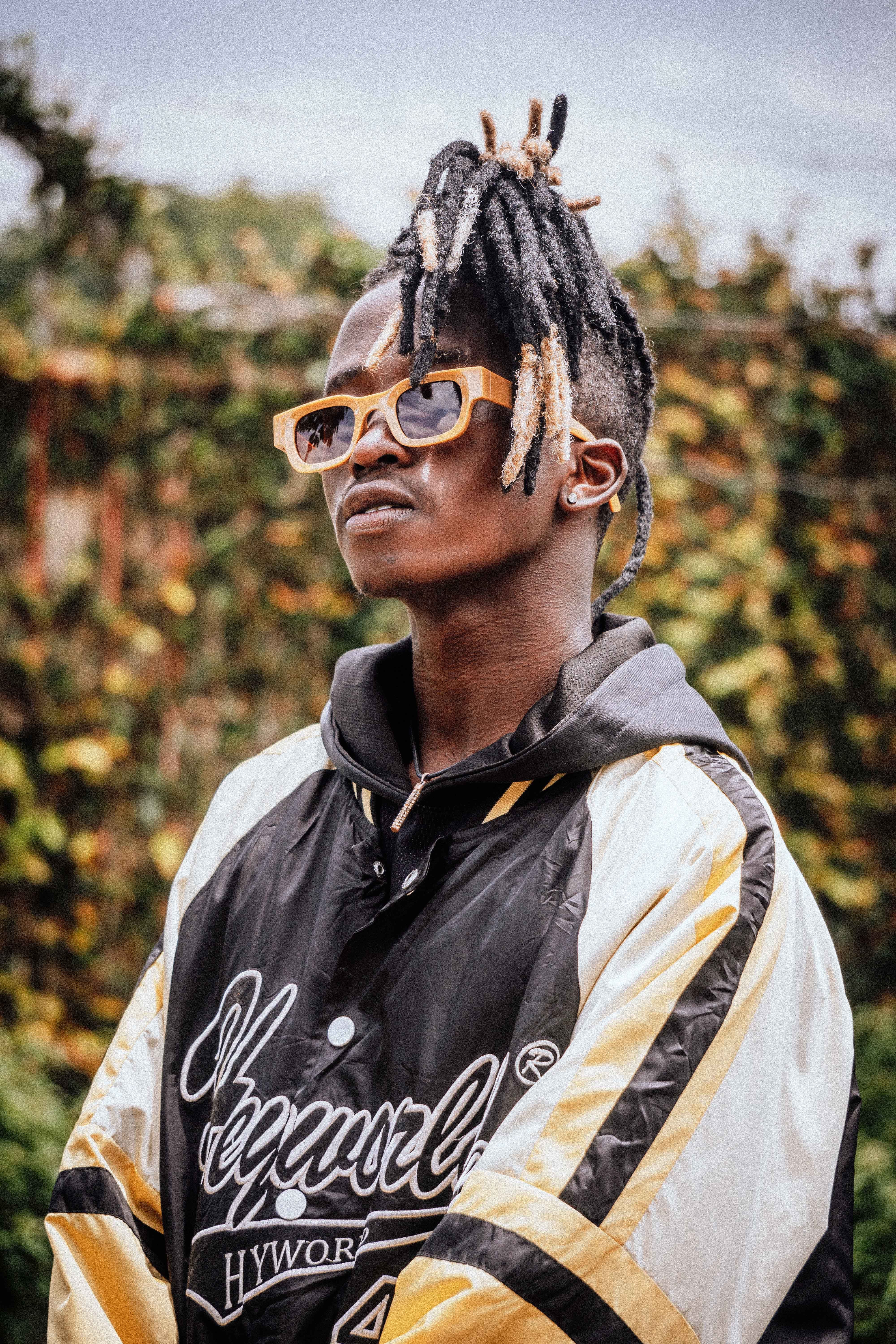 Fashionable young man with dreadlocks wearing a stylish jacket and sunglasses outdoors.