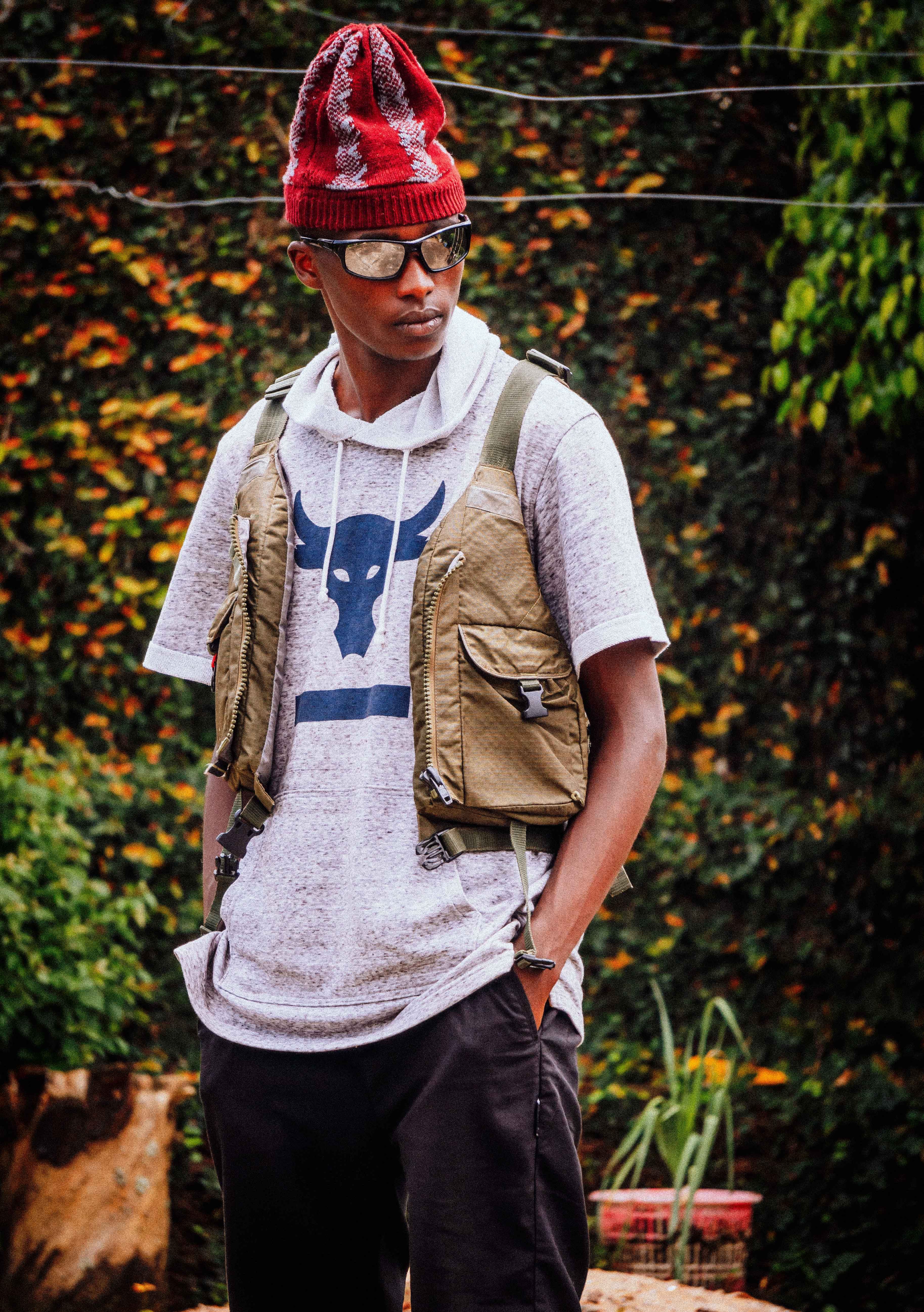 Young man posing outdoors in a casual outfit featuring a red hat and sunglasses, projecting a fashionable, relaxed vibe.