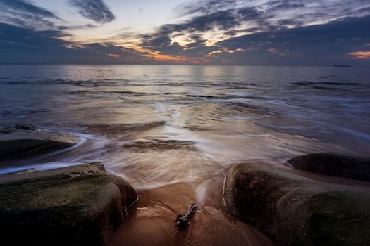 Tranquil beach sunset with gentle waves over rocks, creating a serene seascape.