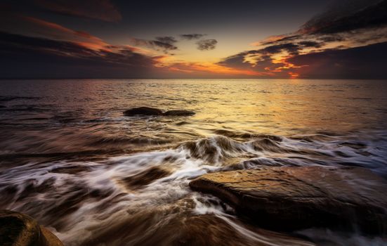 Captivating sunset scene with waves crashing on rocks by the sea, creating a dramatic view.