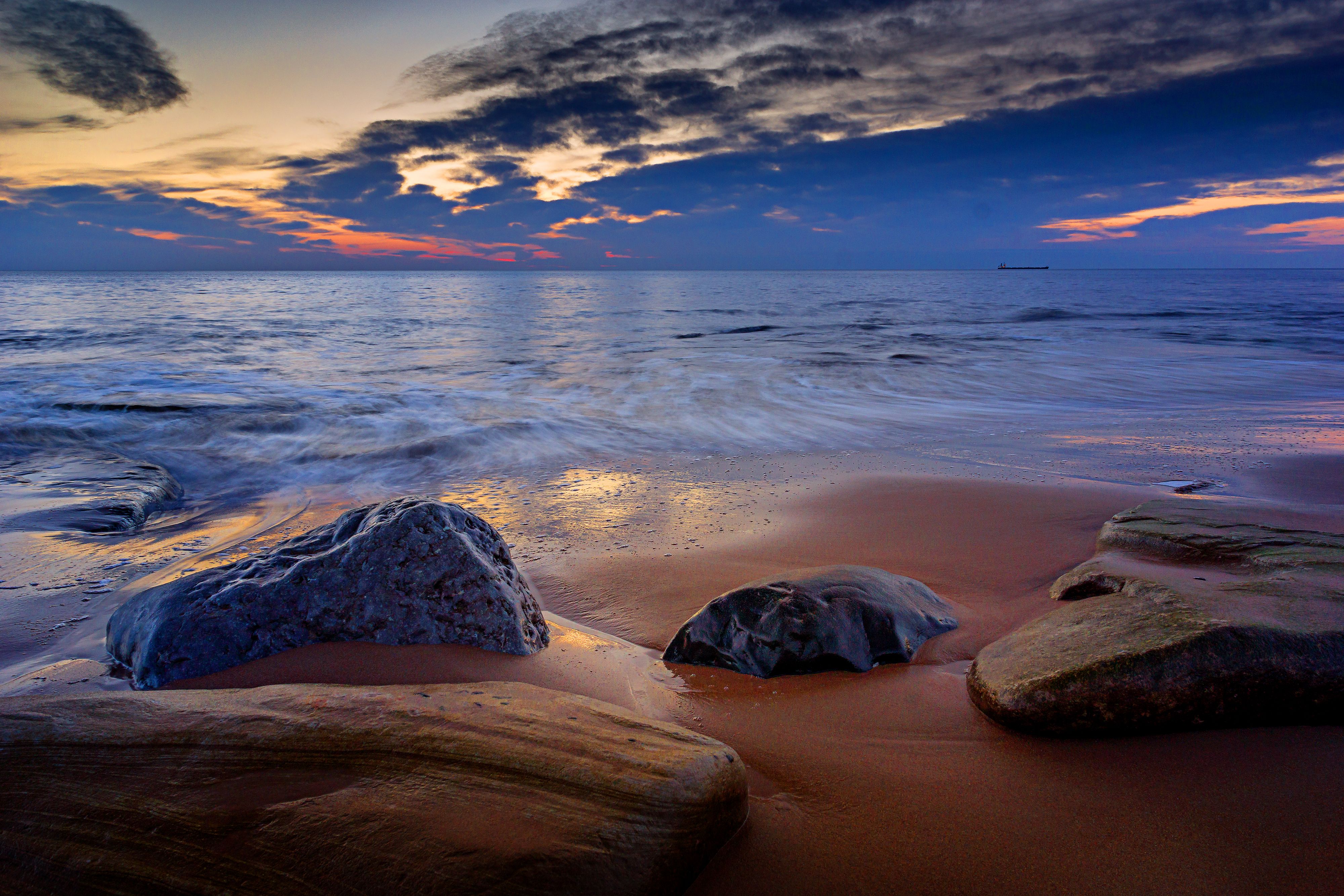 A beach with rocks and water at sunset · Free Stock Photo