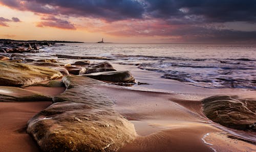 A sunset over the ocean with rocks and sand