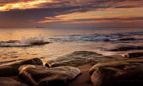 A sunset over the ocean with rocks and water