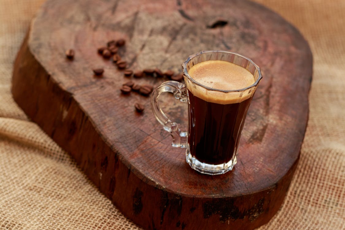 A glass of coffee sits on top of a wooden stump
