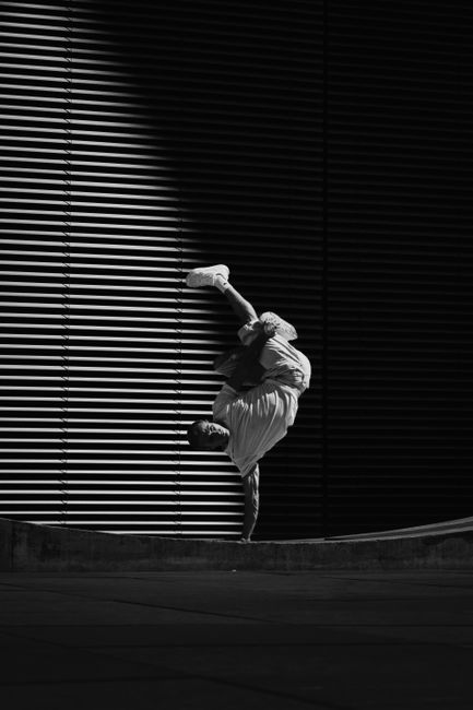 Black and white photo of a breakdancer performing an upside down handstand against a wall.
