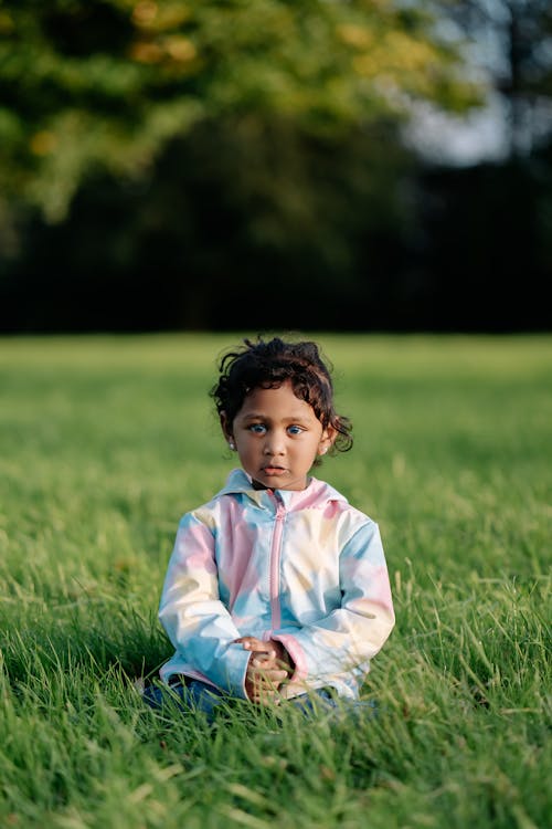 A young child sitting in the grass in a field