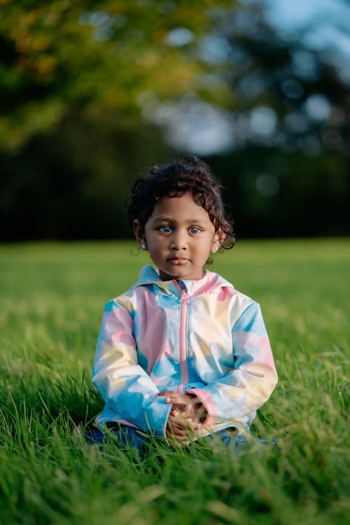 A little girl sitting in the grass in a park