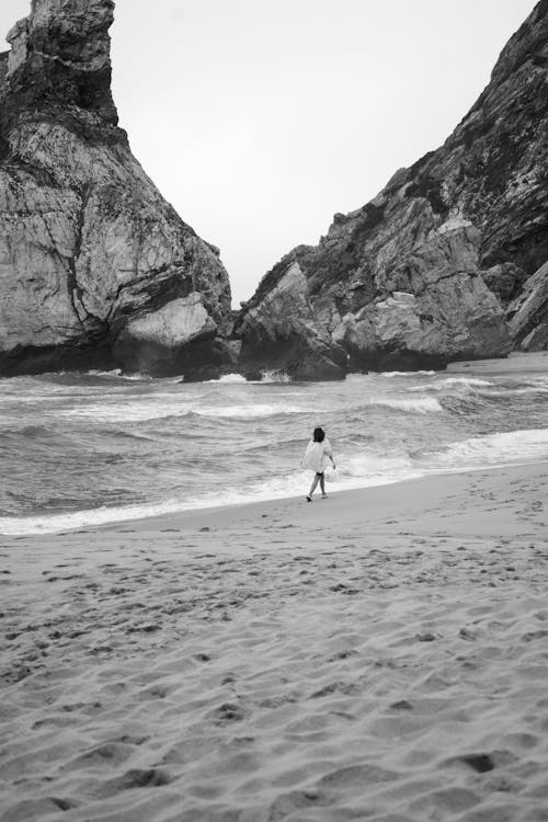 A black and white photo of a person walking on the beach