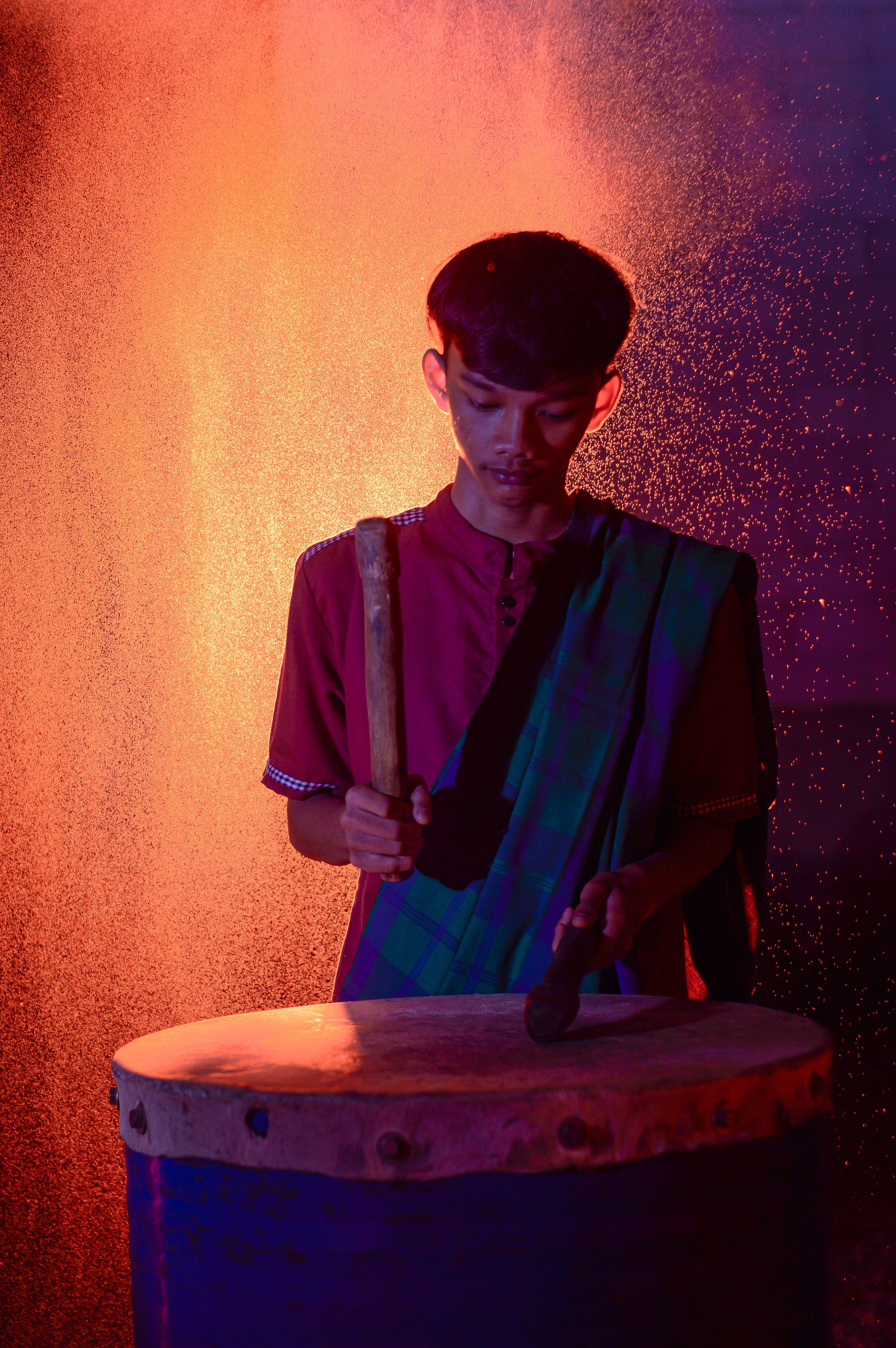 A teenage drummer plays passionately against a dramatic orange backdrop, creating a vibrant scene.