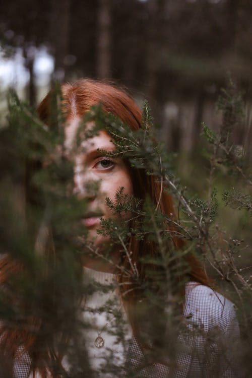 Young Redhead Standing behind Branches Outside 