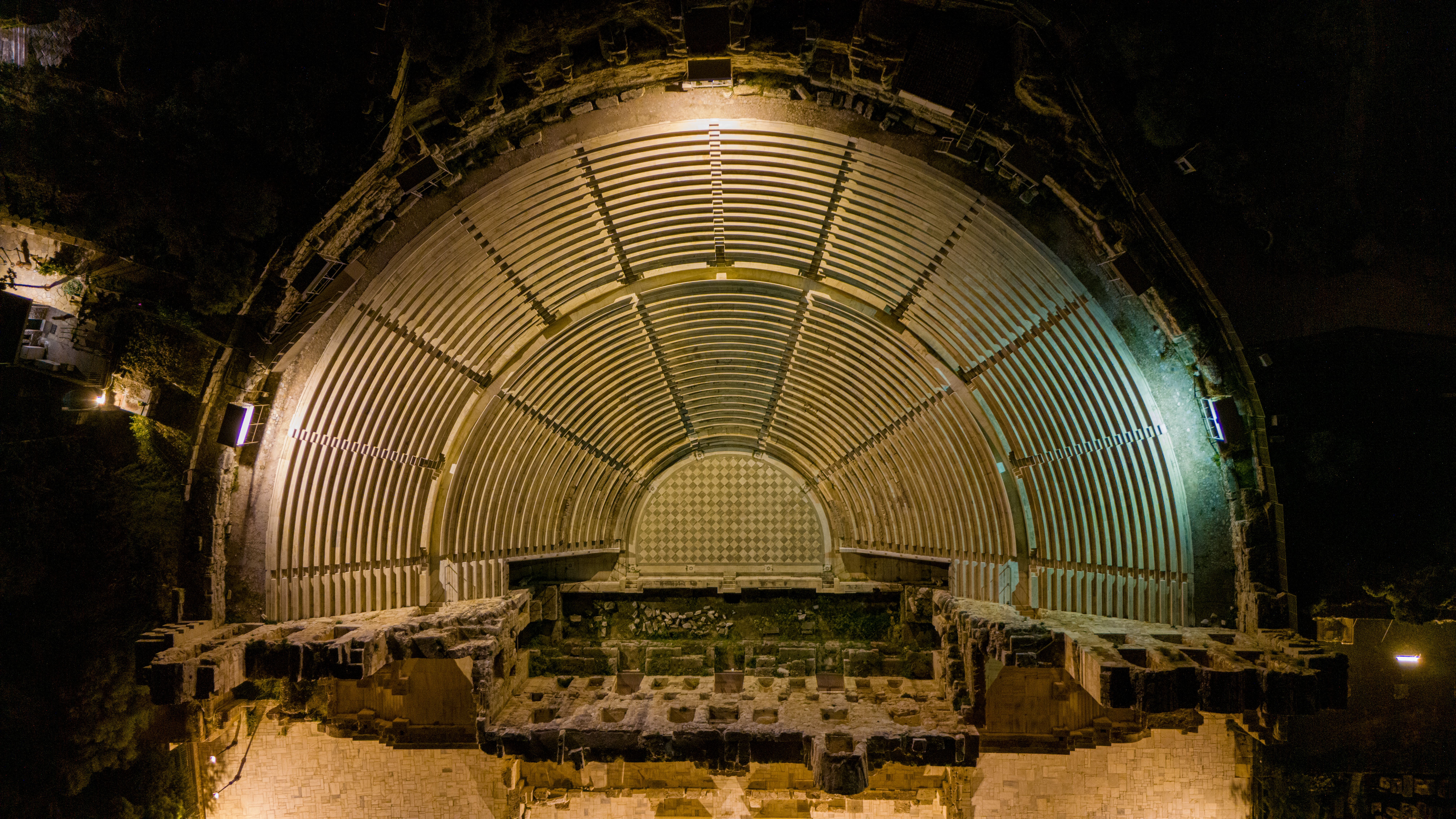 Stunning aerial view of an ancient amphitheater in Athens, illuminated at night showcasing historical architecture.